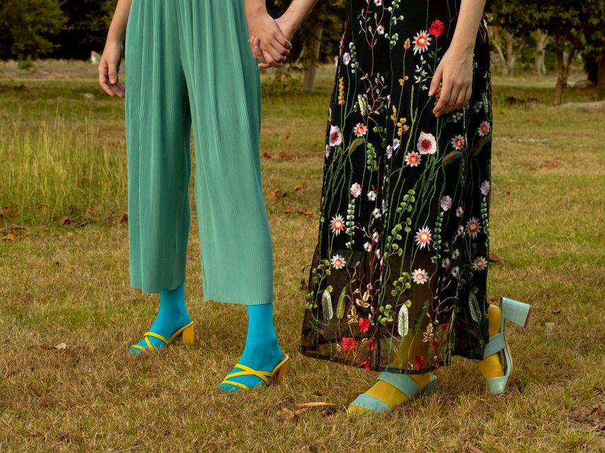 Two women holding hands, showcasing colorful fashion in a grassy outdoor setting.
