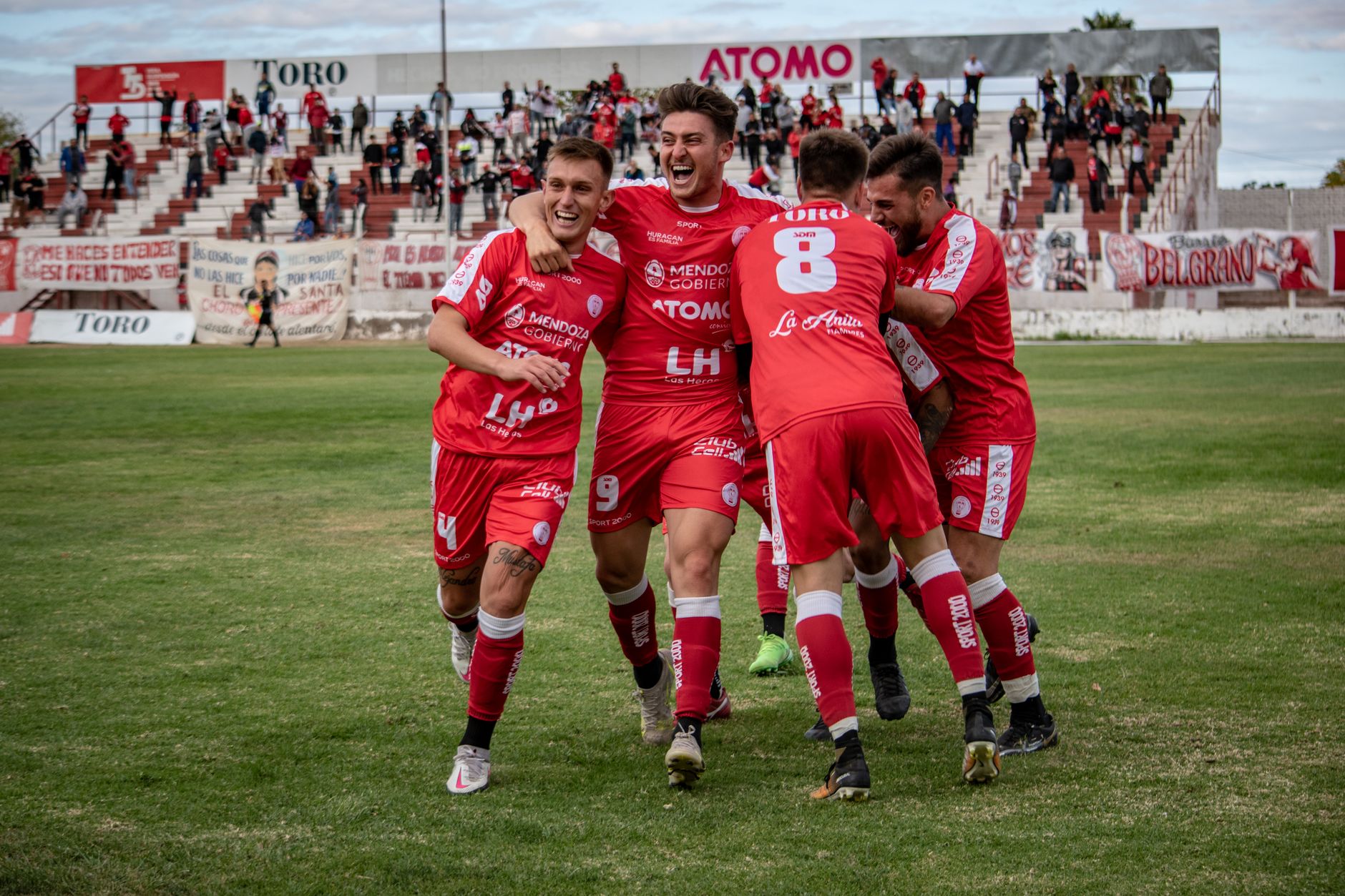 Soccer players celebrating a goal on the field with fans in the background.