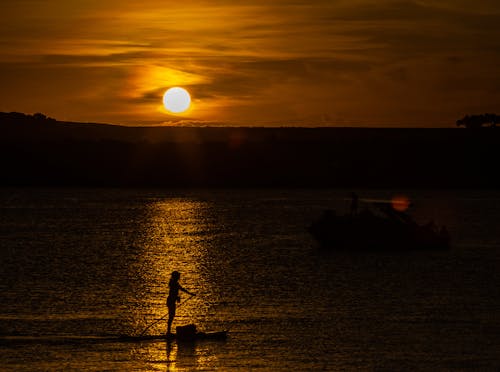 Silhouette of Person Standing on Canoe on Lake at Sunset