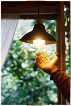 A hand reaching towards a glowing lamp indoors by a window, creating a serene ambiance.