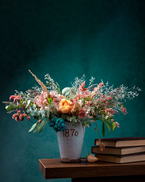 Free Vibrant flower arrangement in retro vase on wooden table with books. Stock Photo