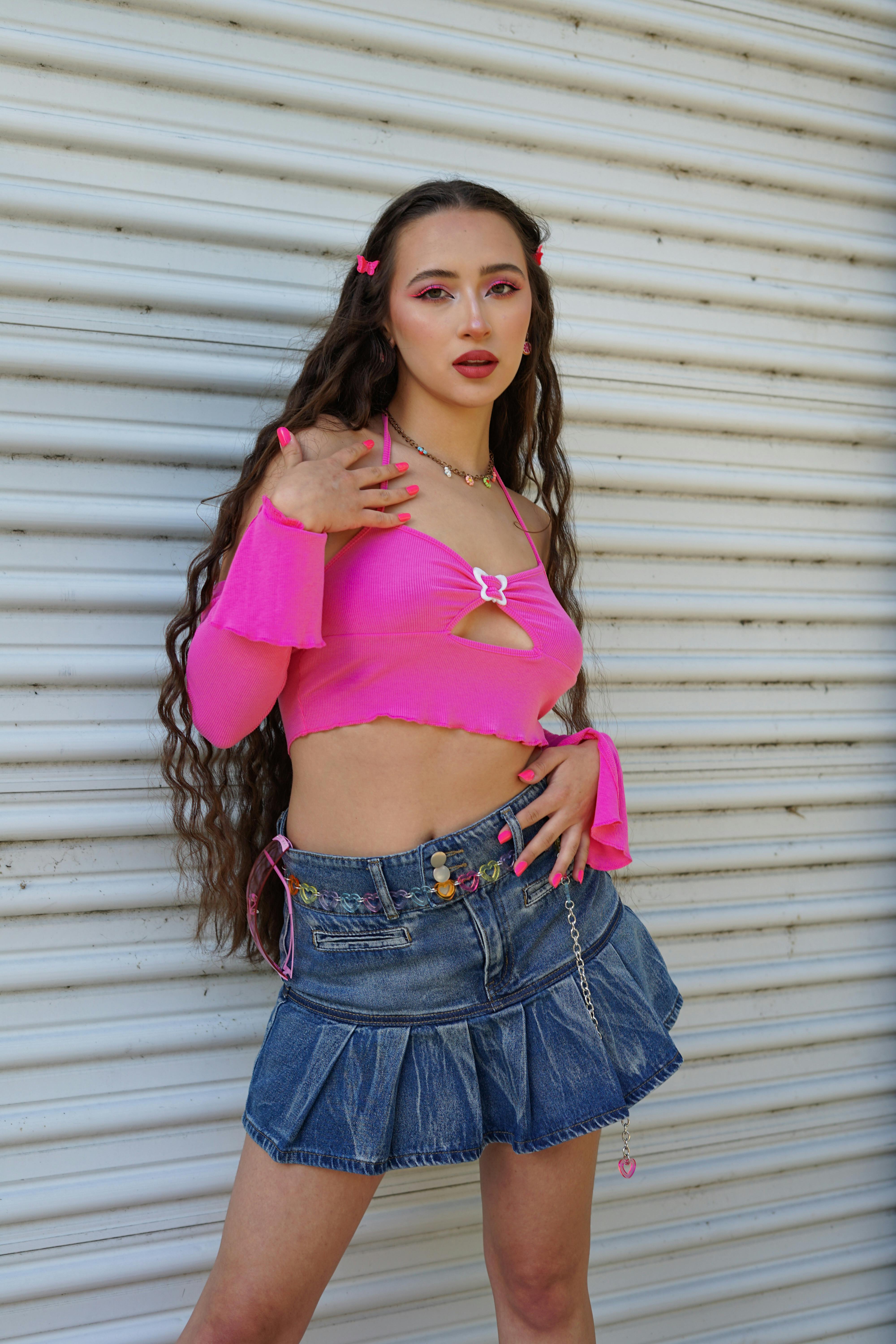 Young woman posing in a vibrant Y2K style outfit with a pink crop top and denim skirt.