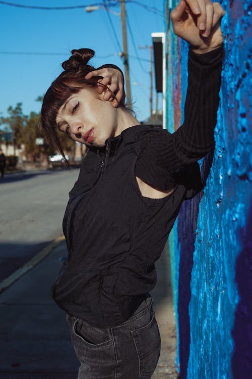 Young Woman with Bangs, Wearing a Black Outfit, Standing on a Sidewalk by a Wall