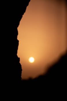 Capture the serene beauty of a sunset silhouetted against the desert horizon in Adrar, Algeria.