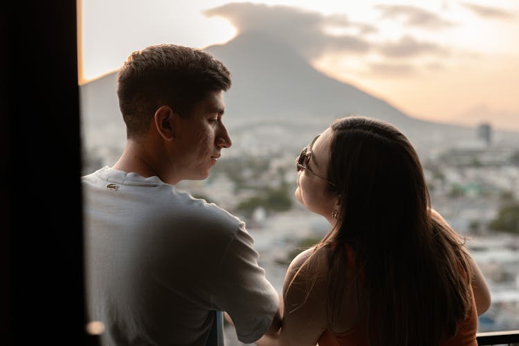 Couple Looking Out Of Window At Mountain In Background