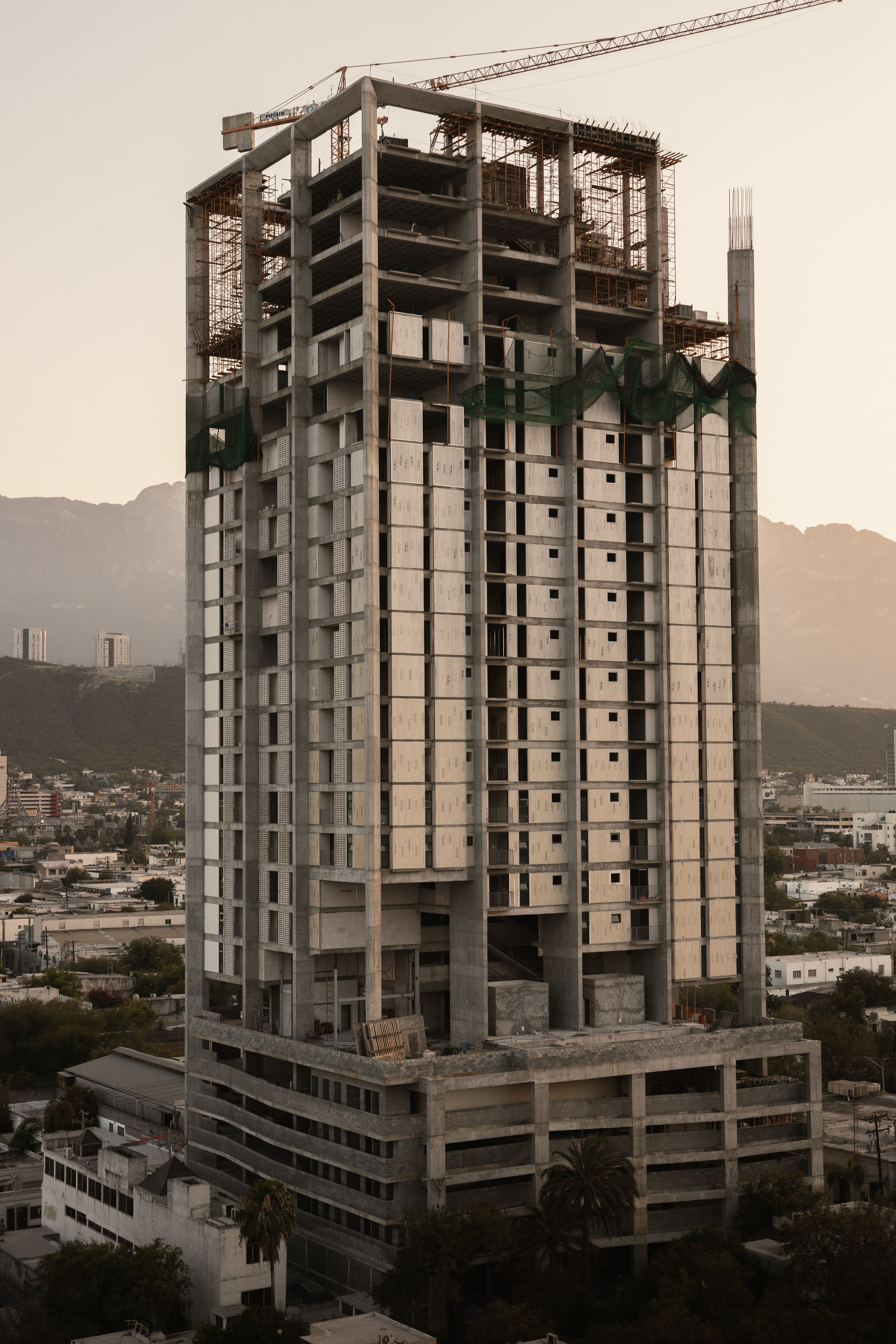 Skyscraper under construction in Monterrey, Mexico, with mountain backdrop at evening.