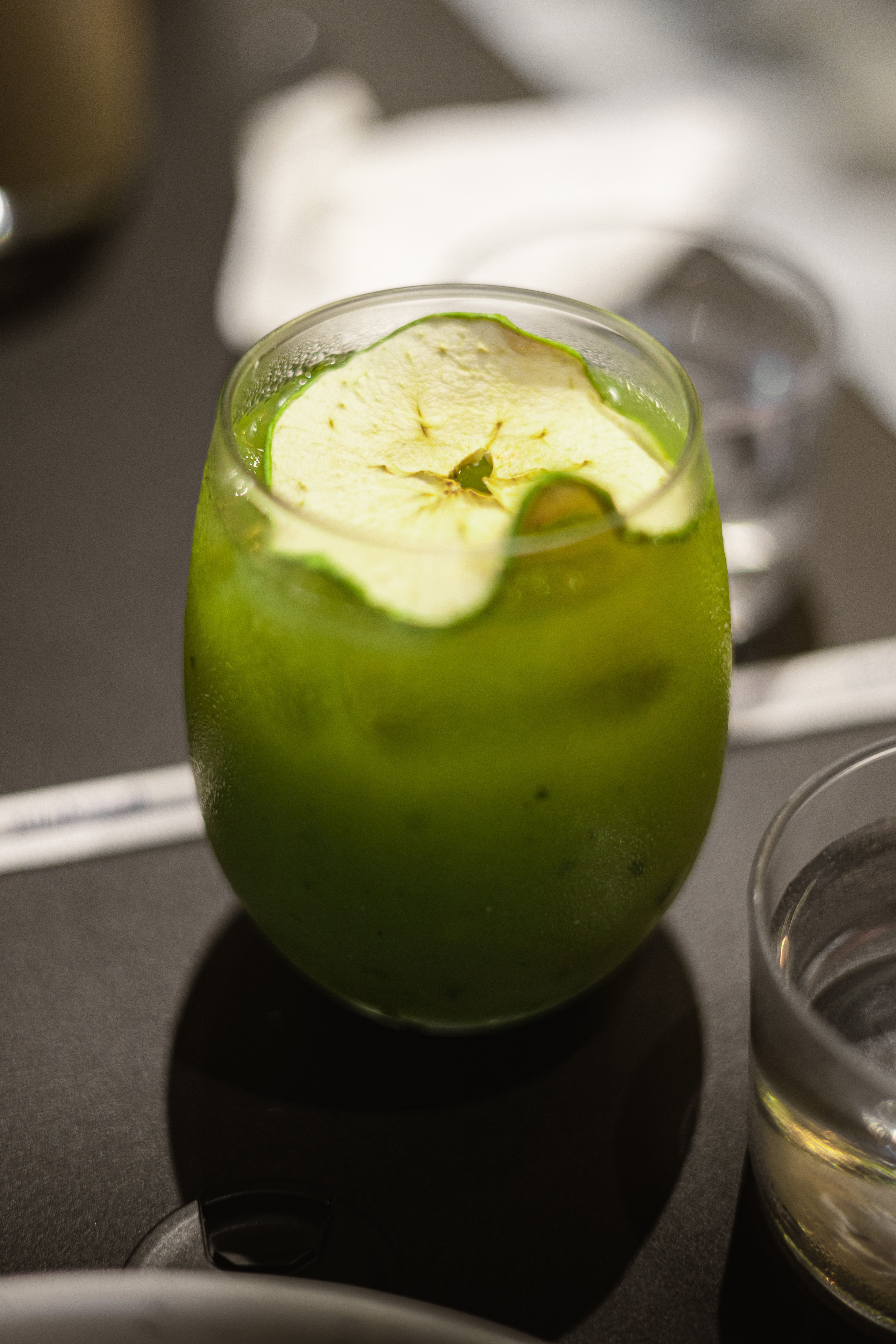 Close-up of a refreshing green apple juice in a glass with a slice of apple on top.