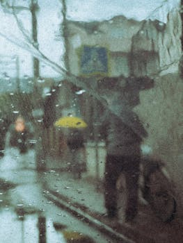 Blurred view of people through rain-splattered window, capturing a rainy day city atmosphere.
