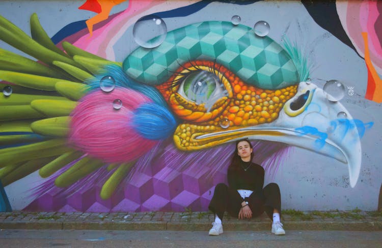 Woman Sitting And Posing By Mural On Wall