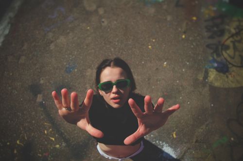 Free Young woman with sunglasses reaching up from graffiti-covered ground. Dynamic and modern perspective. Stock Photo