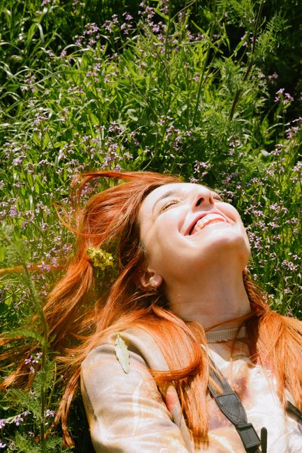 Redheaded woman smiles while enjoying a sunny day outdoors in a field of wildflowers.