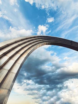 Stunning view of a modern steel arch reaching into a vivid blue sky with dramatic clouds.