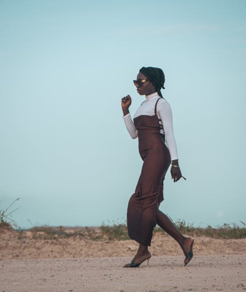 Woman Wearing a Long Brown Dress Walking on Sand in High Heels