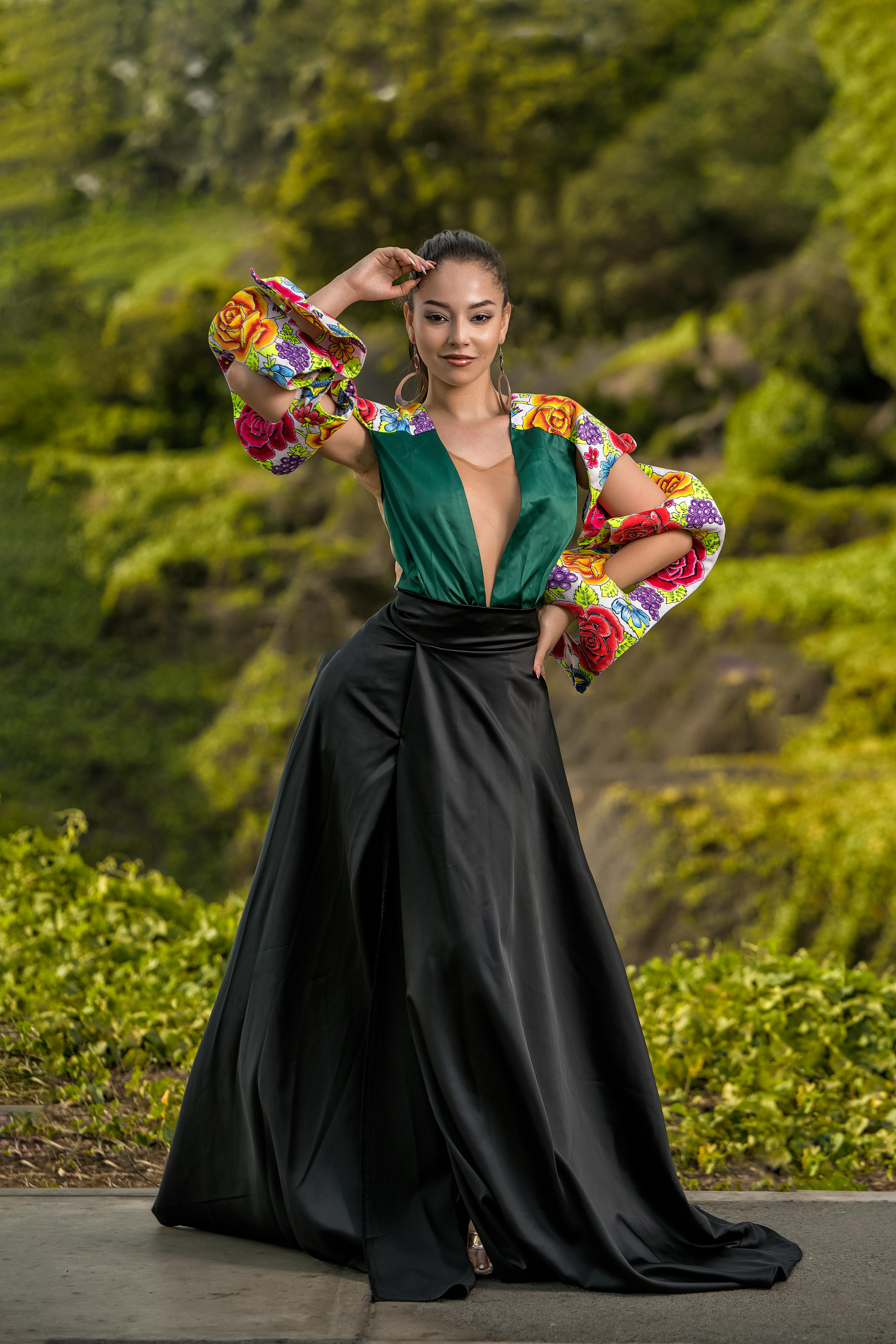 Stylish woman posing in colorful fashion in a lush outdoor setting.