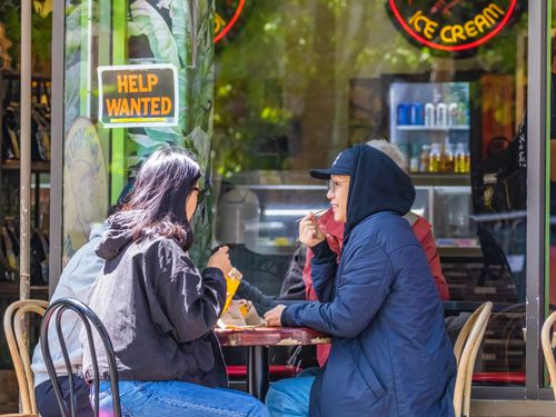 Free Three adults enjoy ice cream and conversation at an outdoor café with a 'Help Wanted' sign. Stock Photo