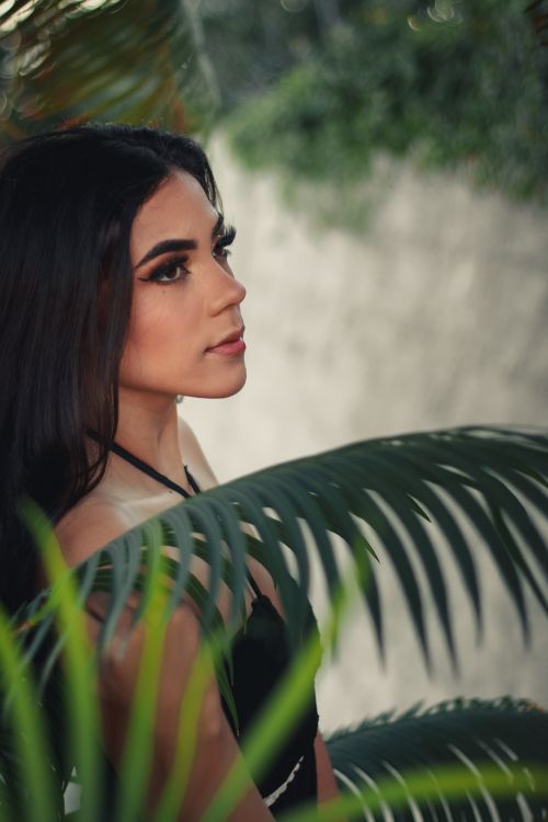 Free Side view portrait of a woman with long brunette hair surrounded by tropical leaves. Stock Photo
