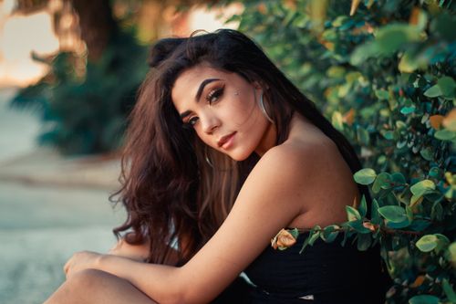 Free Portrait of a woman with brunette hair posing against lush greenery outdoors. Stock Photo