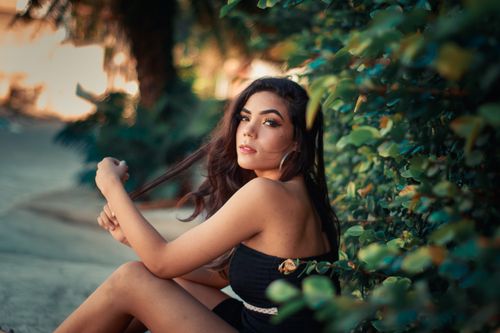 Free Charming woman in a black dress sitting outdoors surrounded by lush greenery. Stock Photo