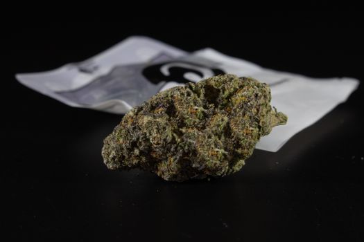 Close-up of a cannabis nugget with packaging, highlighting texture and details against a dark backdrop.