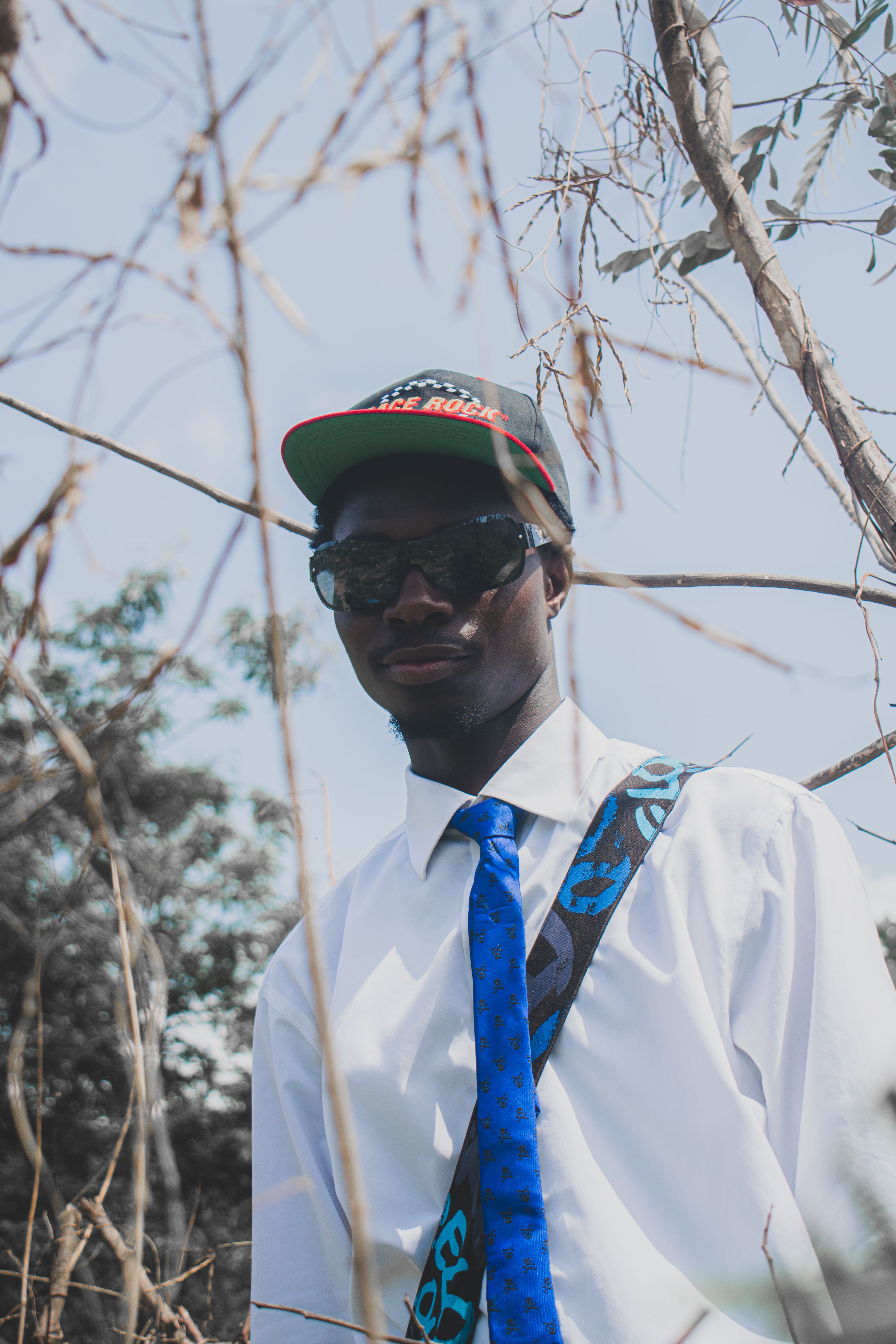 Fashionable man outdoors wearing sunglasses, cap, and blue tie.