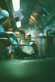 A chef skillfully stirring noodles in a lively restaurant kitchen, captured in Lisbon.