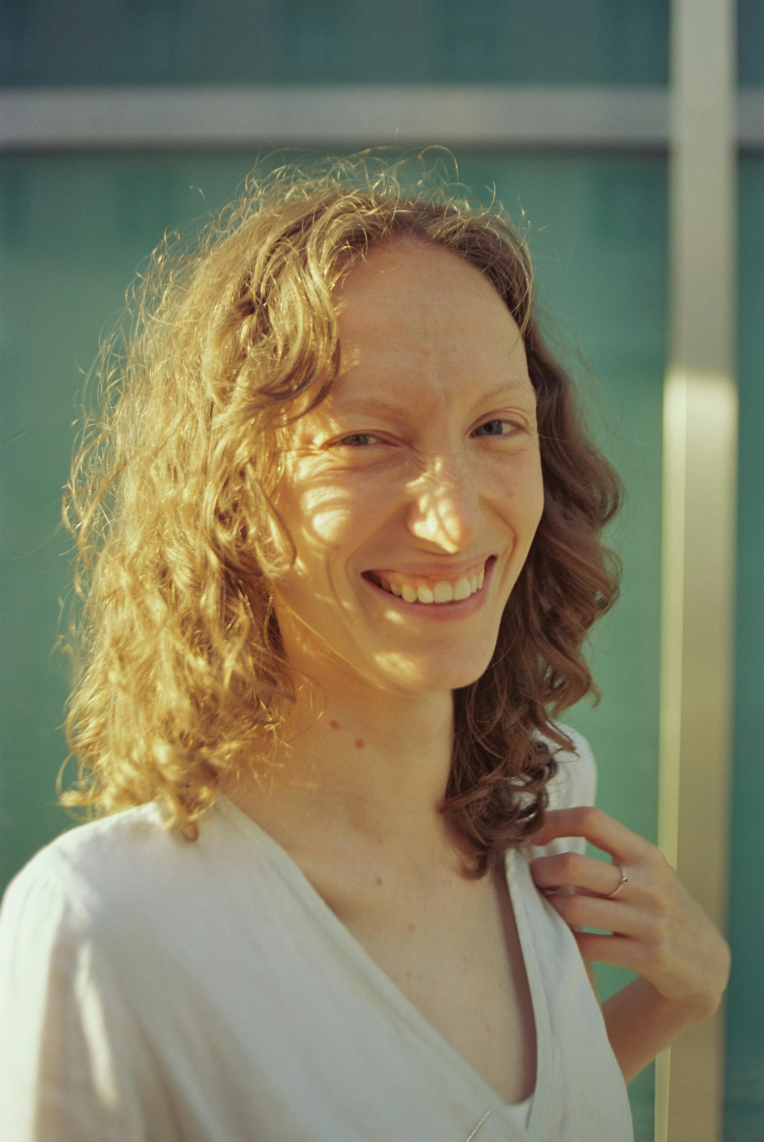 A cheerful woman with curly hair smiles in Lisbon's soft sunlight.
