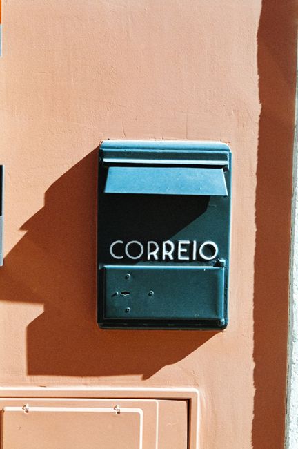 A sunlit Portuguese mailbox affixed to a colorful wall in an urban Lisbon setting.