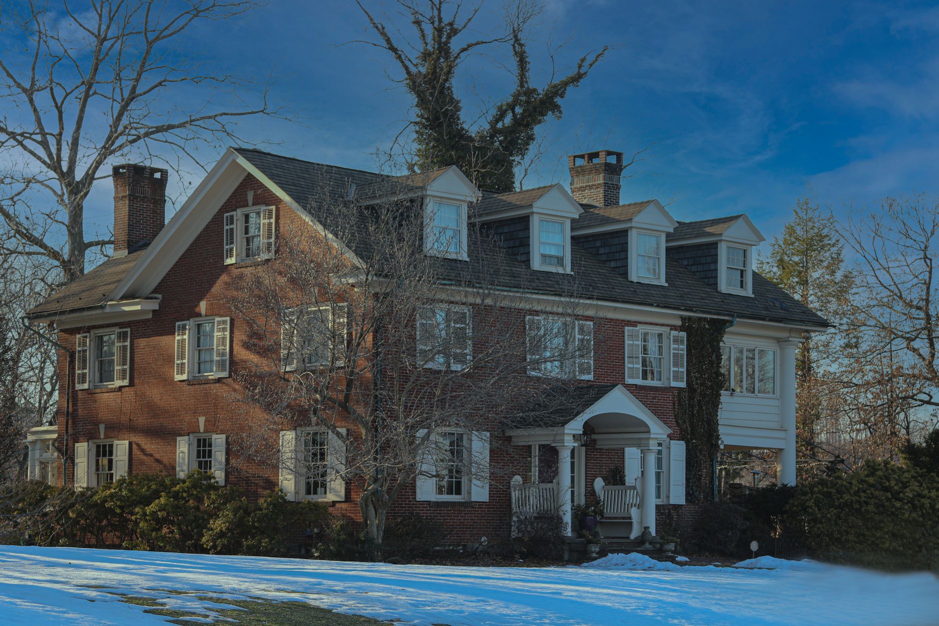 Charming brick house in a snowy suburban setting under a bright blue sky.
