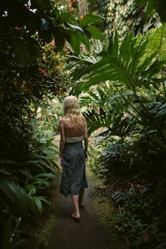 Rear view of a woman walking barefoot through a lush tropical jungle in Hawaii, surrounded by dense foliage.