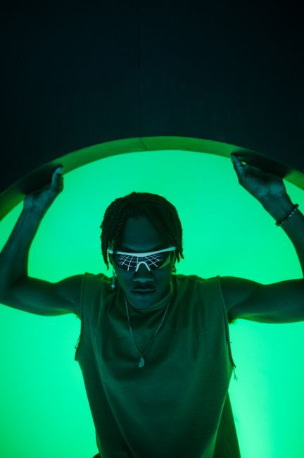 A man poses with futuristic sunglasses under green lighting creating a silhouette effect.