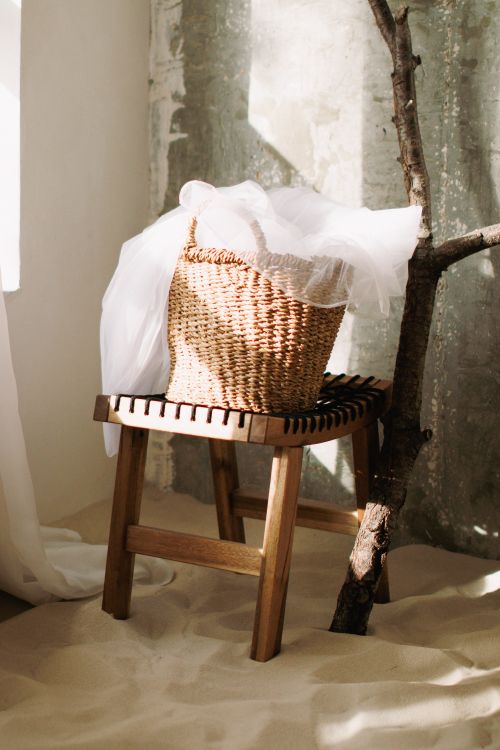 Free Wicker basket on a wooden stool surrounded by sand and tree branch. Stock Photo