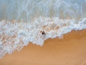 一张航拍照片从高角度拍摄了海滩上的人，海浪正拍打着沙滩