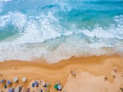 五颜六色的阳伞在沙滩上，海浪冲击上岸，营造出宁静的夏日景象