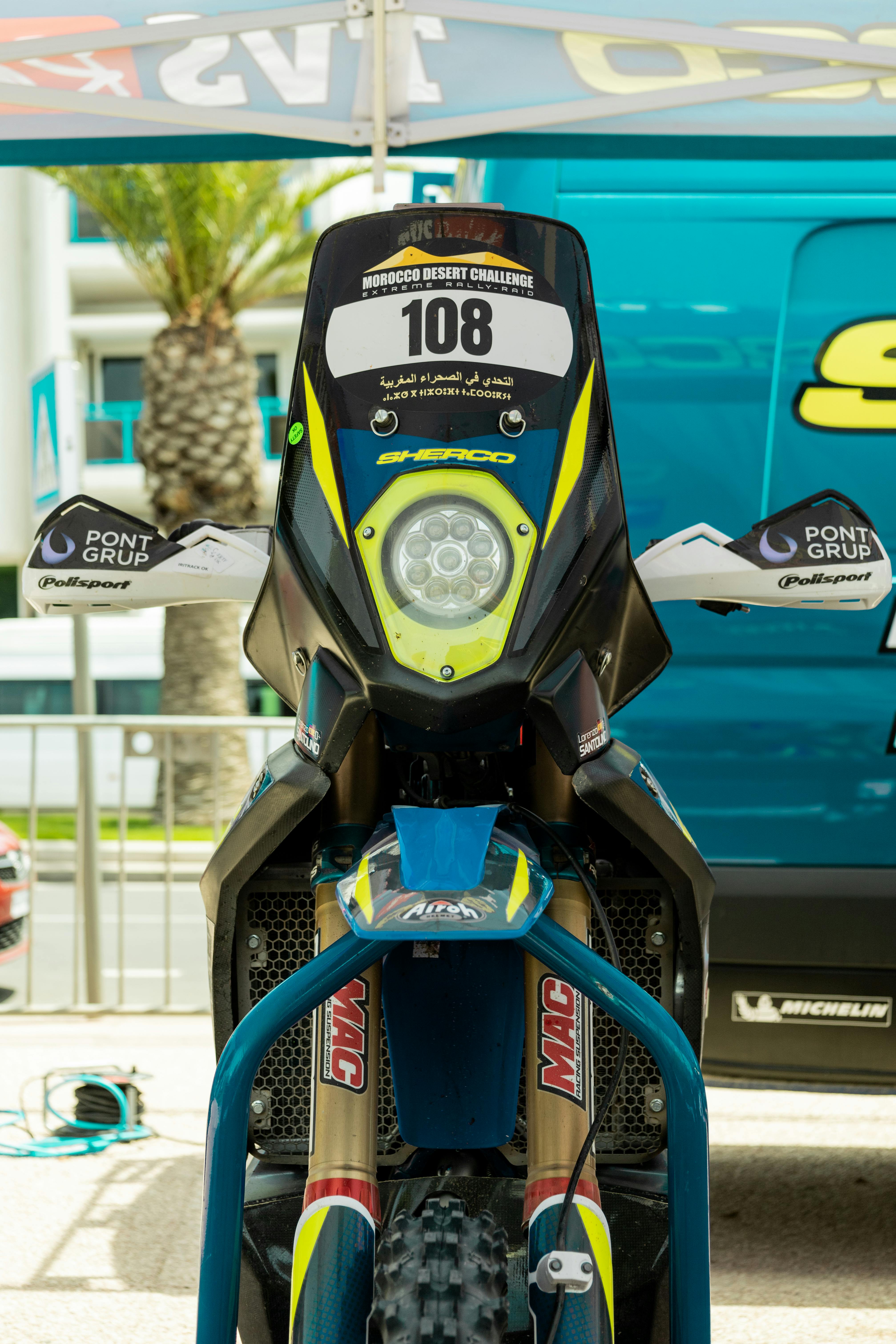 Front view of a rally bike with a racing number and navigation equipment in an outdoor setting.
