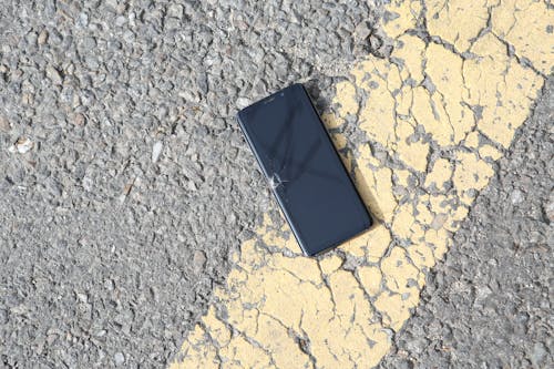 Damaged Cellphone Lying Down on Sunlit Asphalt