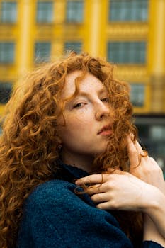 Captivating portrait of a red-haired woman with curly hair against a yellow building background in Kyiv, Ukraine.