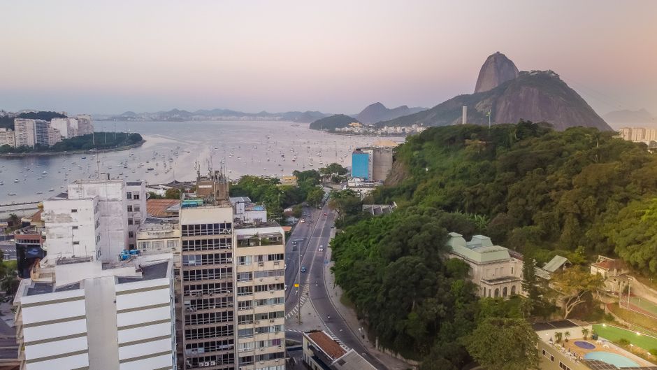 Stunning aerial view of Rio de Janeiro’s coastline, highlighting the iconic Sugarloaf Mountain and urban landscape at sunset.