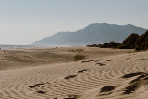 Free Peaceful beach scene in Antalya, Türkiye, featuring footprints in the sand and a scenic mountain backdrop. Stock Photo