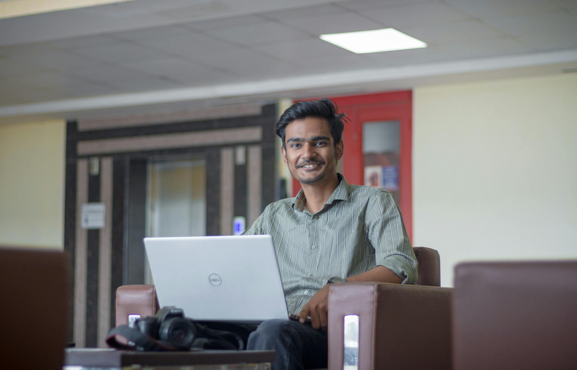 Smiling young man working on a laptop indoors, representing modern freelance lifestyle.