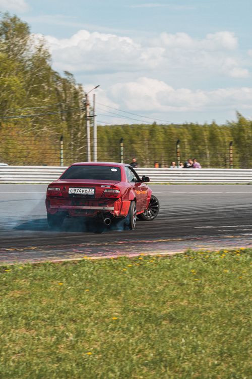 Free A red sports car performs a drift maneuver on an outdoor race track amidst a sunny day. Stock Photo