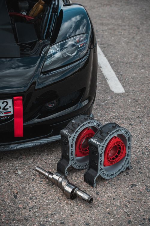 Free Detailed view of car engine parts on asphalt near a black sports car, showcasing automotive maintenance. Stock Photo