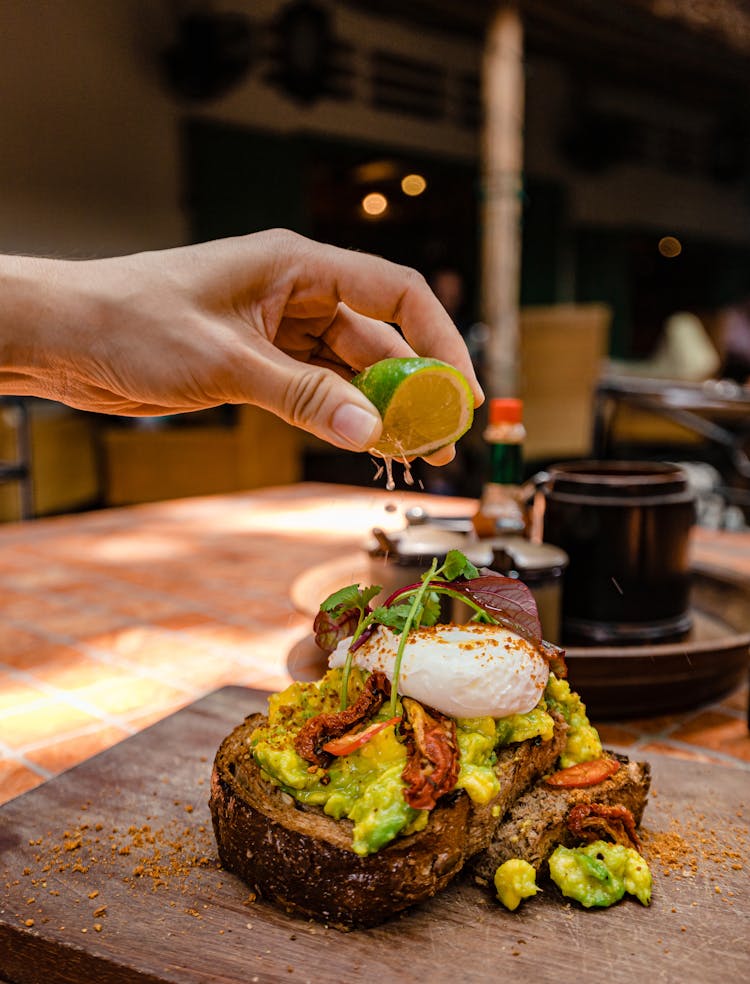 Close-up Of Person Squeezing Lime Juice On An Avocado Toast 