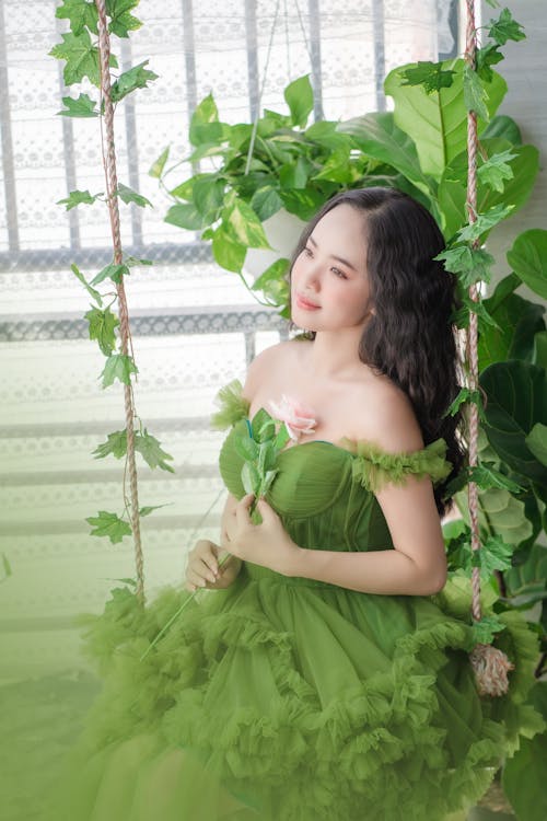 Young Woman in a Green Dress Sitting on a Swing with Flowers