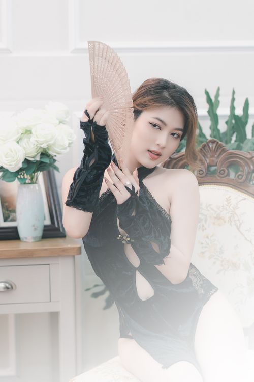 Free An Asian woman in black lingerie posing gracefully with a fan in a bedroom setting. Stock Photo