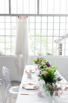 Bright and elegant indoor wedding setting with a long table and hanging wedding dress.