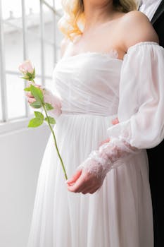 A bride in an elegant white dress holding a rose, symbolizing romance and love.