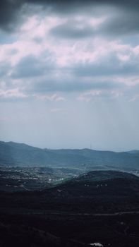 A stunning aerial view showcasing a landscape of rolling hills under an overcast sky with sunbeams breaking through.