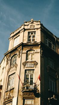 Old tenement building facade with ornate balconies and flags on a sunny day.