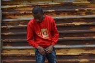 Stylish young man posing in red sweatshirt against a rustic metal wall.