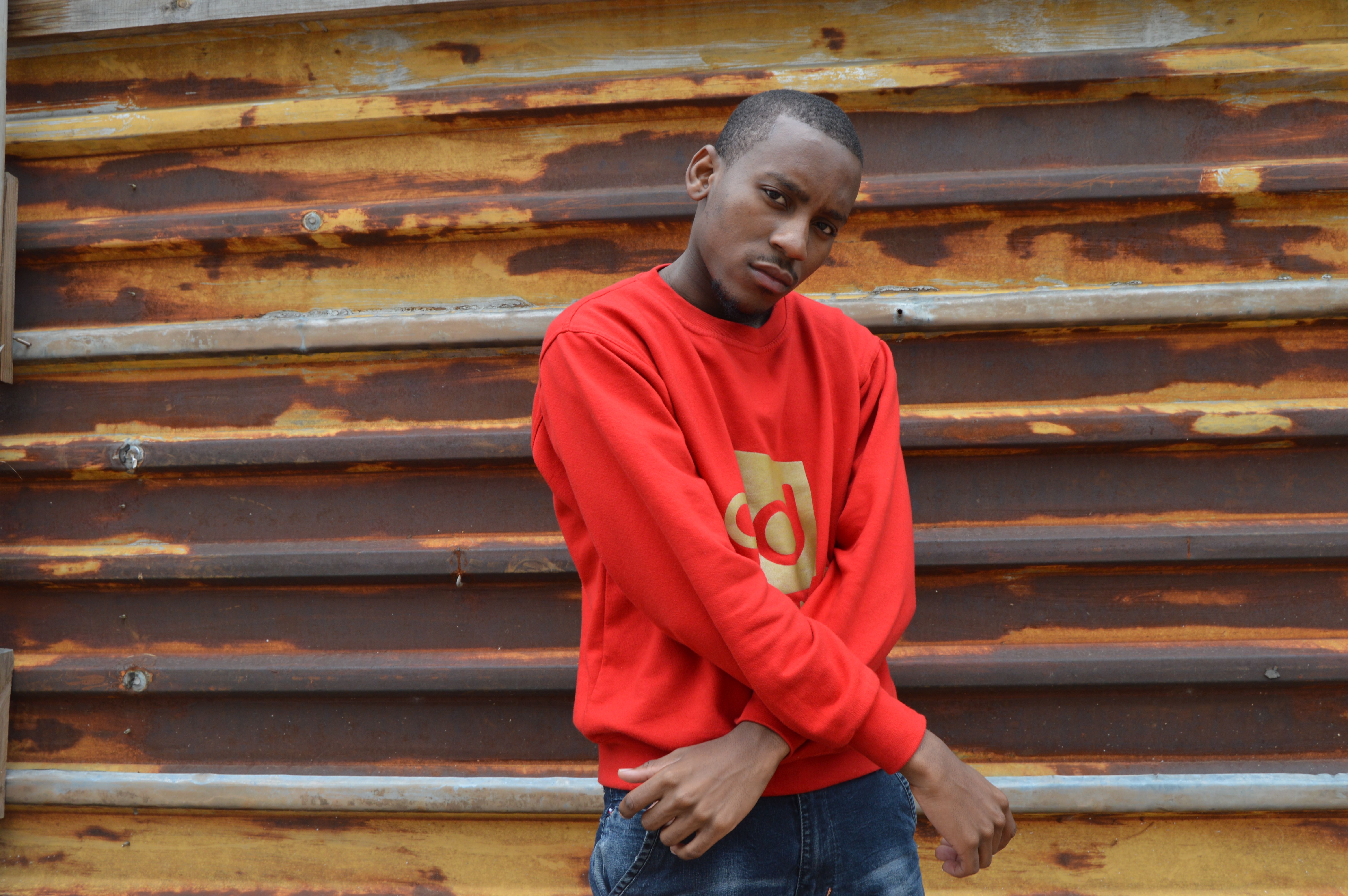 Stylish urban portrait featuring a man in a red sweater posing against a rustic wall.